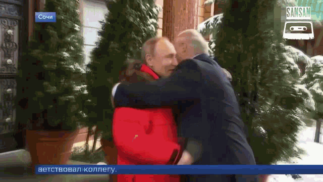 a man in a suit is hugging another man in front of a sign that says sansan