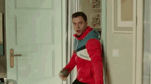 a man in a red and blue jacket is standing in front of a door .