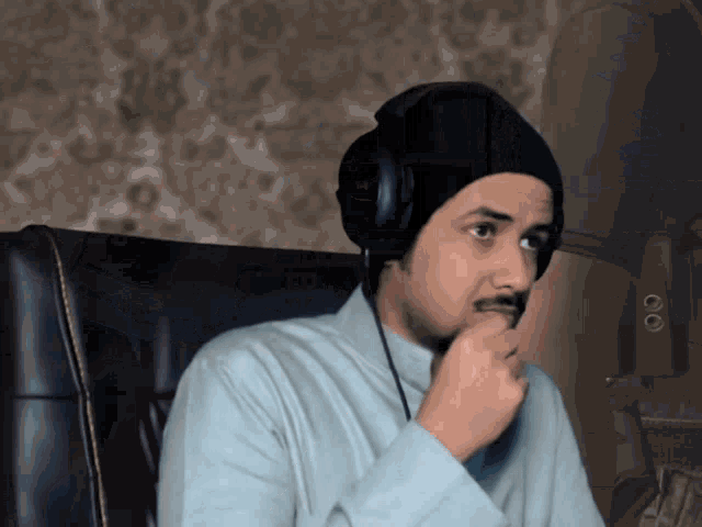 a man wearing headphones and a beanie is sitting in a chair with his hand on his chin