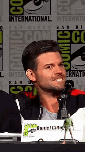 a man sitting at a table with a sign that says comic con