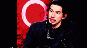 a man with a mustache is sitting in front of a red background with a circle in the middle .