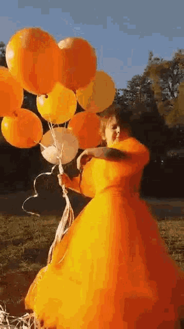 a girl in an orange dress is holding a bunch of orange balloons .