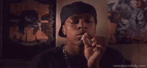a man is smoking a cigarette in front of a wall with a painting on it .