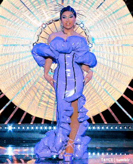 a woman in a purple dress is standing on a stage with a fan in the background .