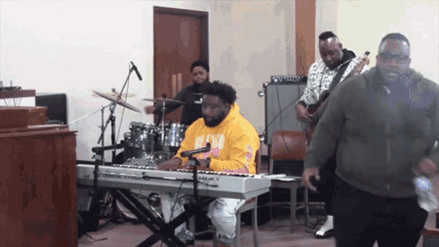 a man in a yellow hoodie is playing a keyboard in front of a band