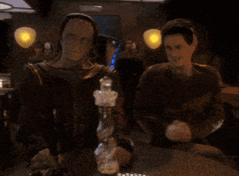 a man in a leather jacket is drinking from a glass in a dark room