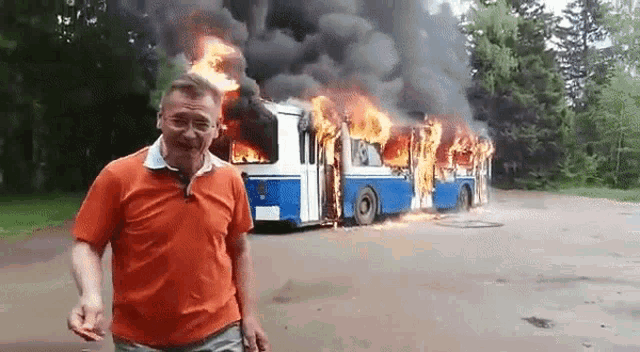 a man in an orange shirt stands in front of a burning bus