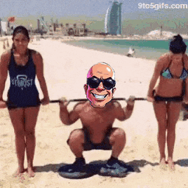 a man squatting on the beach with two women behind him .