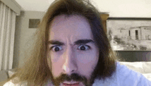 a man with long hair and a beard is making a funny face while looking at the camera .