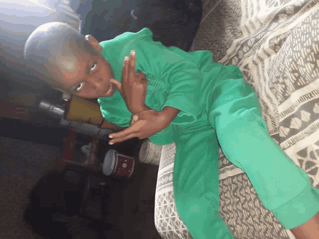 a young boy in green pajamas is laying on a bed and making a funny face
