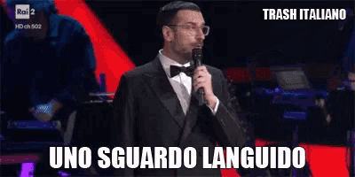 a man in a tuxedo is holding a microphone and says uno sguardo languido