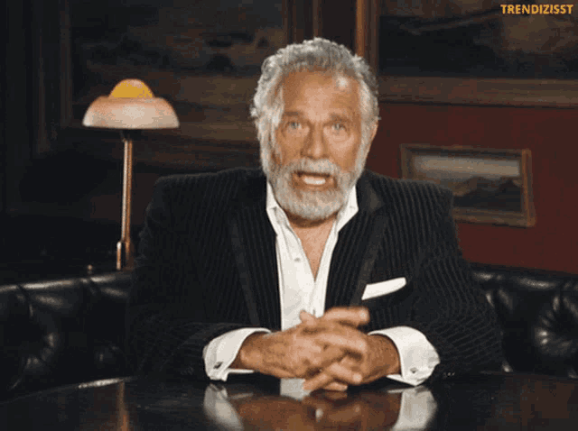 a man in a suit is sitting at a table and laughing with the words trendizisst above him