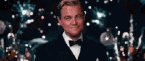 a man in a tuxedo and bow tie is standing in front of a crowd of people .