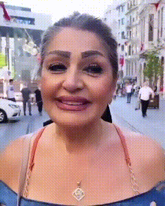 a woman wearing a blue top and a necklace is smiling on a street