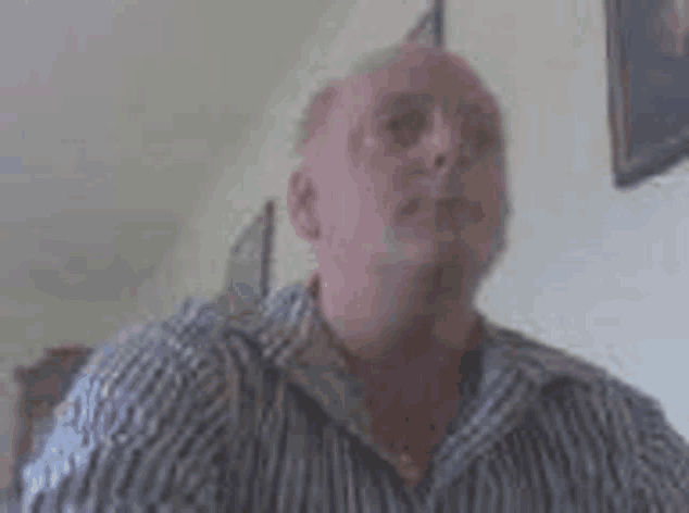 a man in a striped shirt is smoking a cigarette in a room .