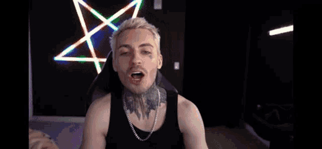a man with a tattoo on his face is giving the middle finger while sitting in front of a pentagram .
