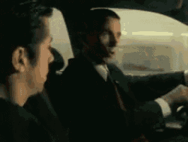 two men in suits are sitting in a car talking