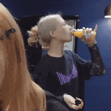 a woman wearing a black shirt with the word dream on it is drinking from a bottle