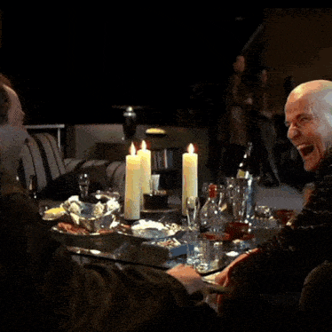 two men sit at a table with lit candles