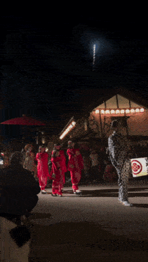 a group of people in red kimonos are dancing in front of a firework display