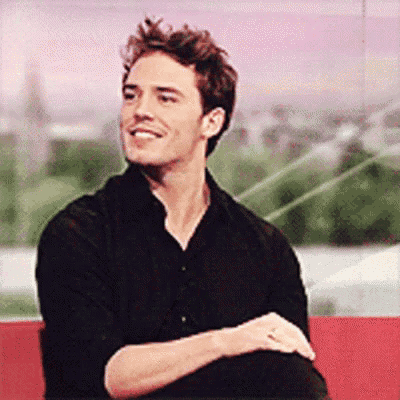 a man in a black shirt is sitting on a red couch with his arms crossed .