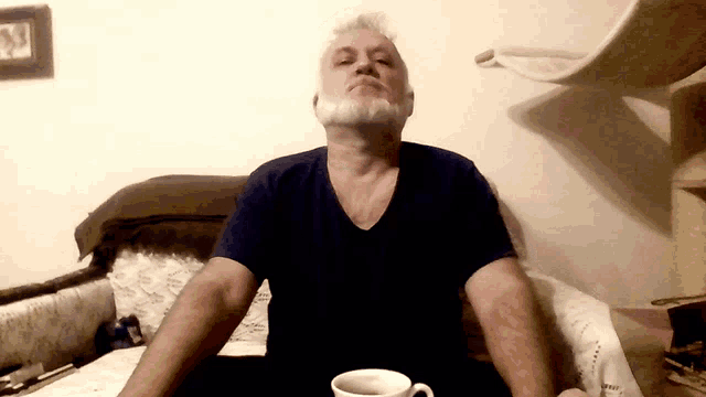 a man with a beard sits in a chair with his eyes closed and a cup of coffee in front of him
