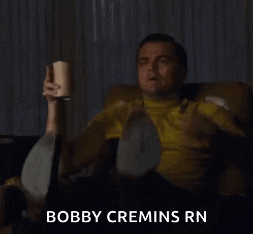 a man is sitting on a couch holding a cup of coffee and pointing at the camera .