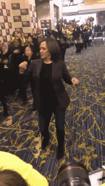 a woman in a black jacket is dancing in front of a crowd in a room with the number 311 on the wall