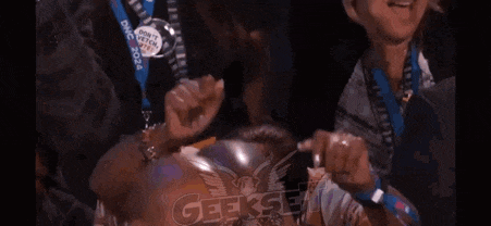 a group of people are sitting in a stadium watching a game and a woman is making a funny face .