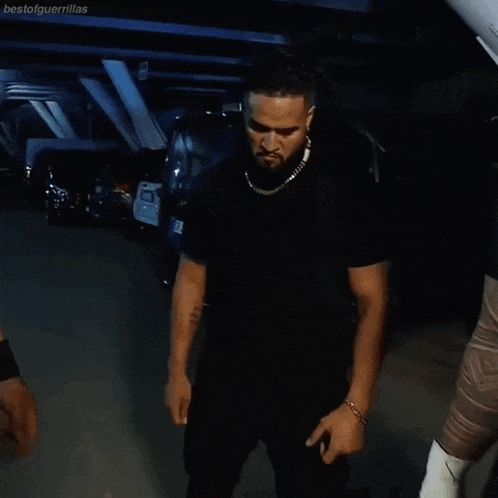 a man in a black shirt with a gold chain around his neck is standing in a parking lot