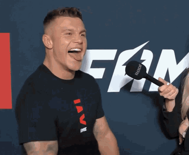 a man sticking his tongue out while holding a rode microphone in front of a sign that says fan