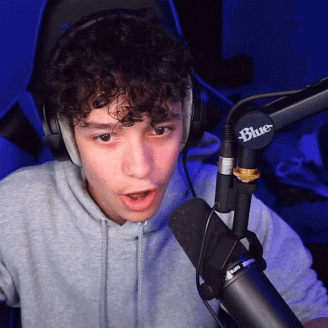 a young man wearing headphones and a blue microphone looks surprised