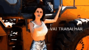 a woman stands in front of a large yellow tractor with the words vai trabalhar written on the bottom