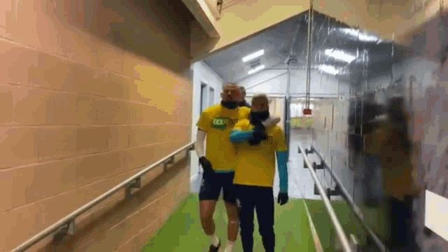 a man wearing a yellow shirt that says tck on it is walking down a hallway