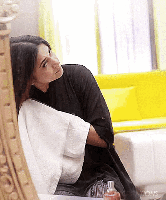 a woman sitting in front of a yellow couch with a bottle of perfume in front of her
