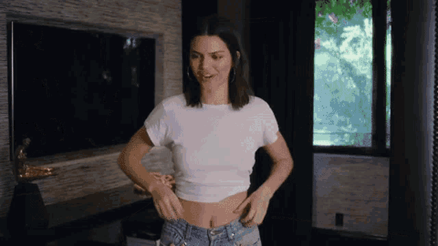 a woman in a white t-shirt and jeans is standing in front of a television .