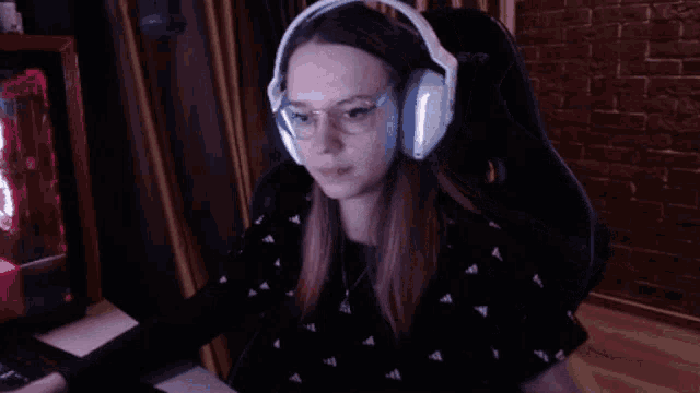 a woman wearing headphones and glasses is sitting in front of a computer monitor .