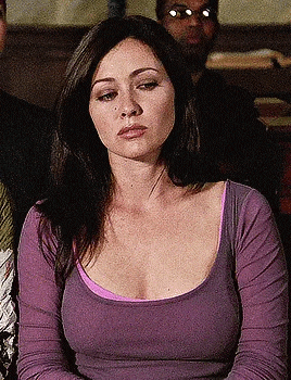 a woman in a purple shirt is sitting in front of a group of people and looking at the camera .