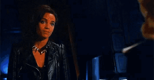 a woman in a leather jacket is standing in a dark room with a man .
