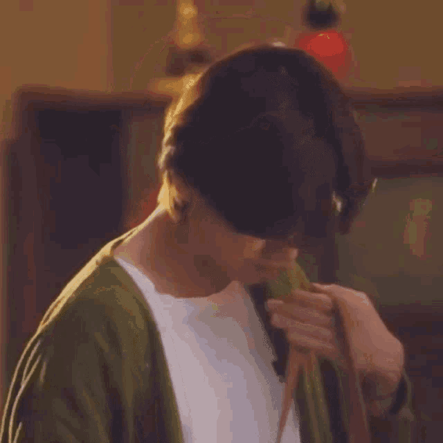 a young man is wearing a green cardigan and a white shirt .