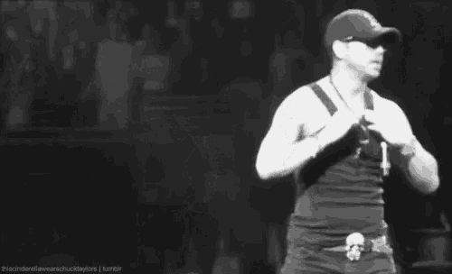 a man is taking off his shirt on a stage while wearing a hat and sunglasses .