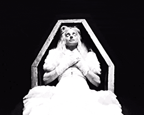 a woman is laying in a coffin with her eyes closed and a ring on her finger .