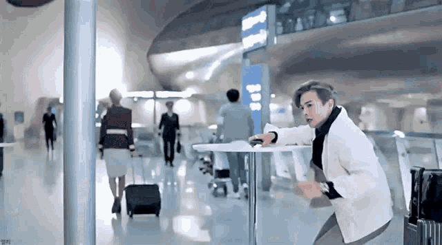 a man is standing next to a table in an airport while people walk by .