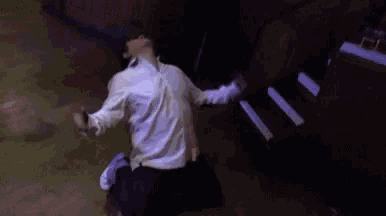 a man is kneeling down in front of a piano with his arms outstretched in a dark room .