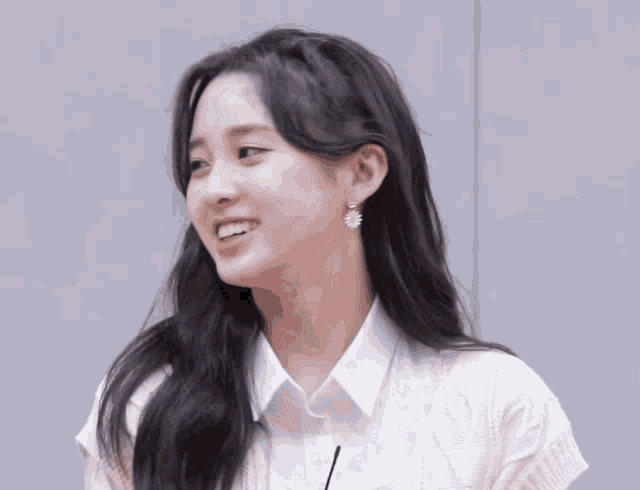 a young woman wearing a white shirt and earrings smiles