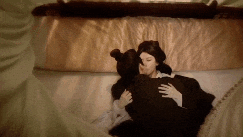 a woman is kissing a man on the cheek while laying on a bed .