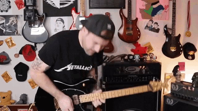 a man playing a guitar with a metallica shirt on