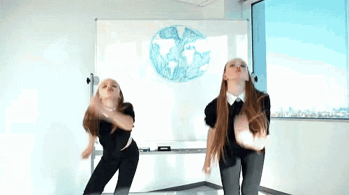 two girls are dancing in front of a white board with a drawing of a globe on it
