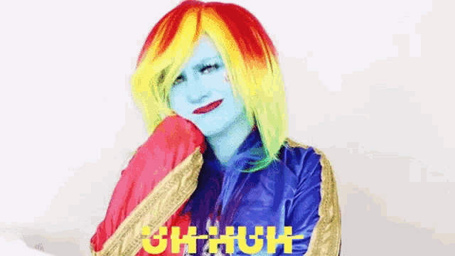 a woman wearing a rainbow wig and a captain marvel costume is smiling .