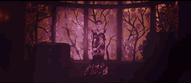 a woman in a black dress is standing in front of a wall with trees on it